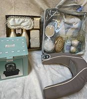 Full view of spa and relaxation items grouped, showing boxed items, transparent carry bag with bathrobe and bath accessories, and massaging pillow.