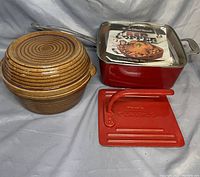 Roaster, griddle press, pottery bowl with lid arranged on cloth.