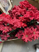 Cardboard box containing multiple silk poinsettia bouquets in bright red, placed on the floor near framed paintings.