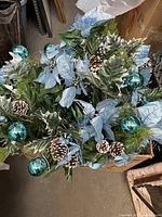 Silk poinsettia mixed bouquets featuring blue poinsettias, green leaves, pinecones, and blue ornaments, displayed in a storage area