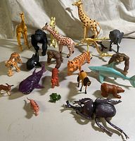 Full assortment of animal and dinosaur toy figurines arranged on light surface showing size and color variations.