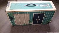 Closed cardboard carrying case for Barbie Dream House, numbered 816, decorated with tree and door graphics, with handle on top.