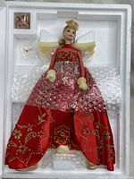 Porcelain Barbie doll in original styrofoam packaging, wearing red and gold embroidered gown with clear overlay and beige hand muffs.