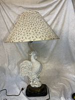 Full view of the vintage rooster table lamp with floral fabric shade on a white draped background.