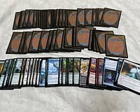 Photo showing rows of Magic The Gathering cards, backs side up on top and fronts displayed below showing various card types and colors.