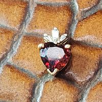 Close-up image showing heart-shaped garnet with diamond baguette accents set in 14k gold against a brown textured surface.