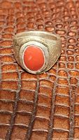 Front view of antique sterling silver ring with red coral cabochon on a textured surface.