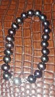 Full bracelet showing natural black pearls and sterling silver clasp on textured brown background.
