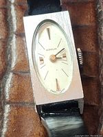 Close-up front image of the vintage ladies watch showing the brushed silver-tone rectangular case and oval white dial with gold-tone hands and markers.