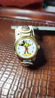 Front view of the wristwatch showing the Mickey Mouse character on the dial with hands as arms and clear legible numerals.