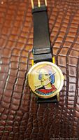 Front view of watch showing Picasso style multicolor dial, gold-tone round case, and black leather strap
