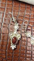Pair of large sterling silver earrings with deep red oval stones laid on textured brown leather background showing front and part profile