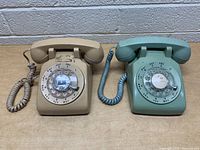 Front view of two vintage rotary dial phones, beige and light blue, showing dial plates and handset.