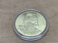 Front view of the gold plated coin inside a clear capsule, showing Jesus' detailed profile.