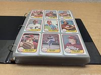 Binder with three-ring holes filled with baseball cards in clear sleeves, showing front sides with player images and team logos.
