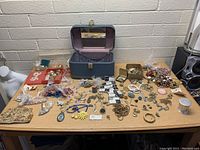 Overview of table spread with blue jewelry case open and assorted jewelry items laid out including chains, bracelets, earrings, pins, and necklaces