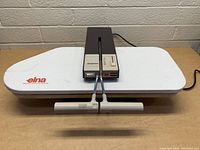 Elna Elnapress iron press with white pressing board, control unit, and handles front view.