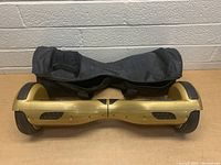 Gold hoverboard with carrying bag placed behind it, showing overall length and side view.
