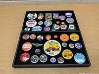Two views of a tray of assorted collectible buttons with various designs and themes.