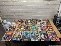 Photo showing a flat lay of 19 assorted comic books from Marvel, DC, and other publishers arranged on a table against a white brick wall.