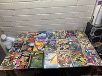Photo showing a table with 25 assorted vintage comics from Marvel and DC such as X-Men, Superman, Batman, Robin, Thing, Catwoman, Nova, Punisher, and Spider-Man.