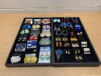 Wide view of two trays displaying various assortments of earrings organized in sections by color and style.