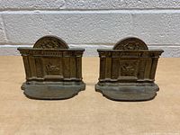 Pair of metal cast iron bookends showing their overall design including fluted columns, central relief, and curved base.