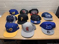 Front view of 11 sports hats arranged on table showing team logos and colors.