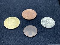 Four novelty coins including Trump coin, Bitcoin, and two other assorted coins on black cloth.