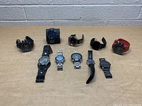 Full lot of 10 assorted watches displayed on a table, showing various styles and colors including black, silver, and red bands.