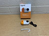 Polaroid Wave underwater streaming camera with box, USB cable, and wrist strap on table surface.