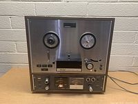 Front view of the TEAC reel to reel tape recorder showing reels, control buttons, VU meters, and power cable.