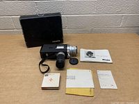 Vintage Minolta Autopak 8 film camera with carrying case and accessories arranged on a table against a brick background.