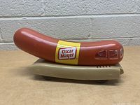 Side angled view of the Oscar Mayer Wienermobile coin bank showing front and side details with logo, wheels and coin slot.
