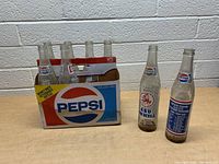 Two vintage Pepsi 16 oz bottles and original 16-bottle Pepsi cardboard carrier for returnable bottles on a table