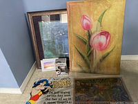 Photo showing two framed artworks (one water scene, one floral), photographic print of sunset, Wonder Woman poster, and boxed Wonder Woman Funko Pop figure.