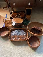 Various woven baskets including oval, rectangular, and round shapes, two wooden bowls, glass votive holder with three compartments, and striped linens folded inside a basket.