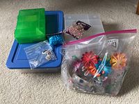 Multiple plastic containers filled with various beads, colorful flower-shaped beads, small bags of crafting beads, and pliers