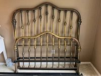Full bed frame including footboard and headboard leaning against a wall, showing the bed frame design with brass spindles and cast iron rounded posts.
