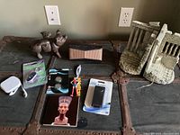 Full lot showing cast iron pig, Bluetooth speaker, key finder, batteries, AirPods, bookends, and collectibles on a metal trunk.