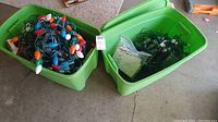Two green plastic bins filled with assorted Christmas light strings including multi-colored large bulbs and smaller clear bulbs.