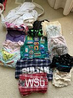 Overview of all clothing items including pajamas, socks, undergarments, and pajama pants in multiple colors and patterns laid on floor.