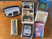 Photo showing two boxed Cross pen sets and various stacks of greeting and note cards with different designs.