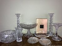 Photo of multiple crystal items including candlestick holders, bowls, vases, coasters, and tray, showing variety and patterns.