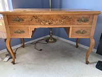 Front view of wooden desk showing carved floral detailing on drawer front and brass handles.