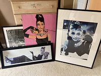 Group of four framed Audrey Hepburn photos and posters arranged on floor showing varying sizes and colors.