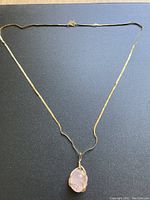 Full view of gold-tone flat chain necklace with pink stone wire-wrapped pendant on dark surface.