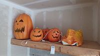 Three electric Jack-o-Lantern pumpkins with carved faces sitting on a wooden shelf.
