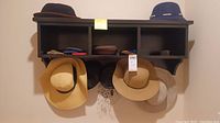 Overview photo of hats on wall shelf with some eyewear cases on top, showing variety of colors and styles.