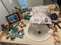 Overview of lot on bathroom countertop including glass ornaments, shells, jewelry, framed stingray art, and tote bag